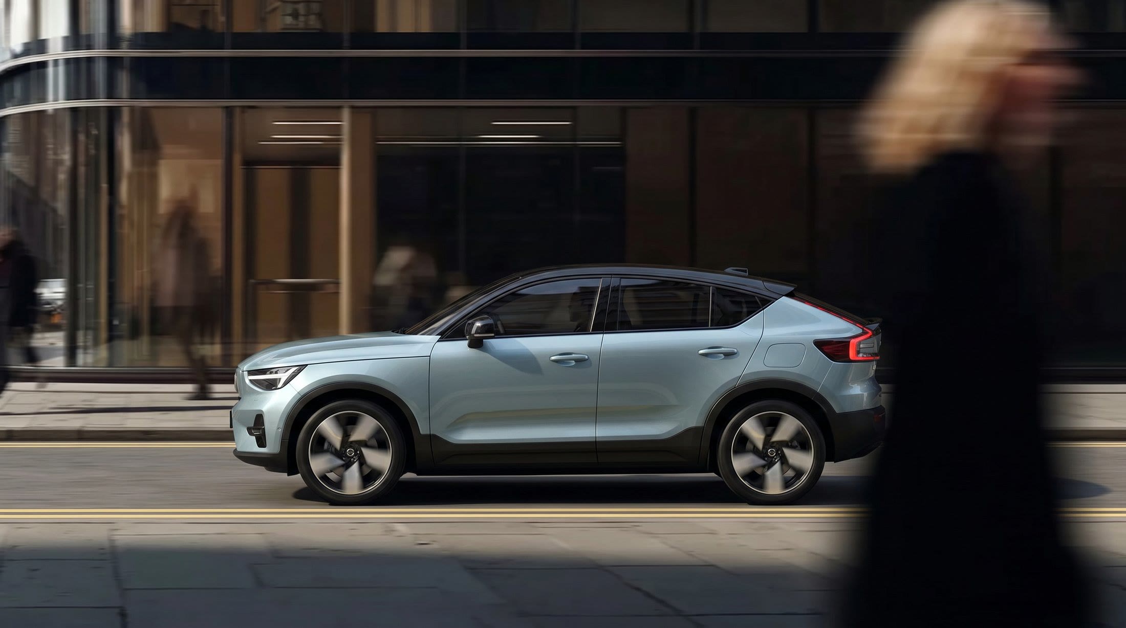 Pale blue crossover passing a glass storefront