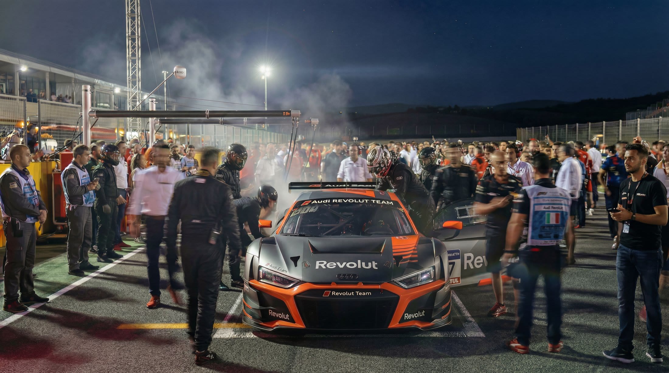 Race car on the grid at night, surrounded by crew